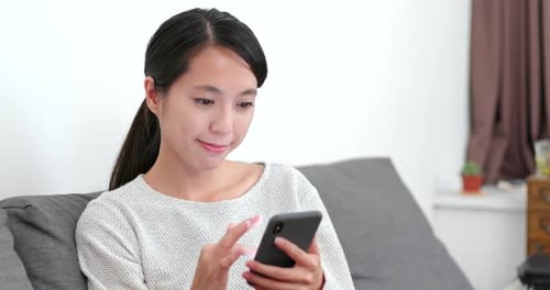 Woman Using Smartphone Relaxing on Sofa Indoors
