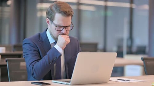 Man in Suit Coughs While Working on Laptop