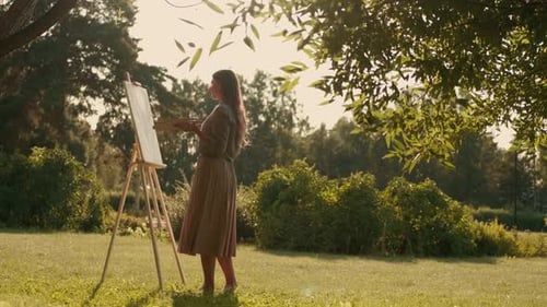 Cheerful Woman Artist Paints a Picture on Canvas While Standing in a Park in Sunny Weather