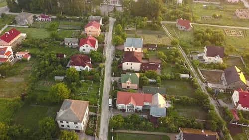 Aerial view of rural residential area with private homes between green fields at sunrise.