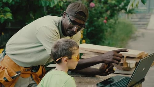 Boy Learning Carpentry From Adult Using Laptop