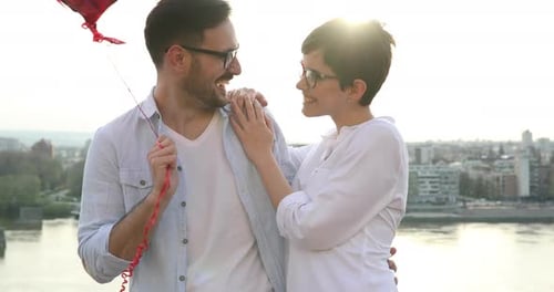 Couple Embracing with Balloons over Cityscape on Sunny Day