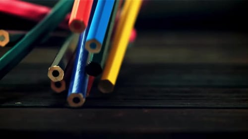 Colorful Pencils Falling onto a Dark Wooden Surface
