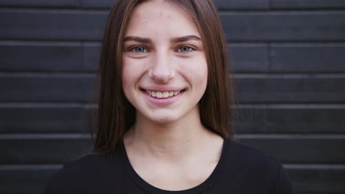 An Attractive Young Lady Straightens Her Hair and Smiles Outdoors. Close-up Shot