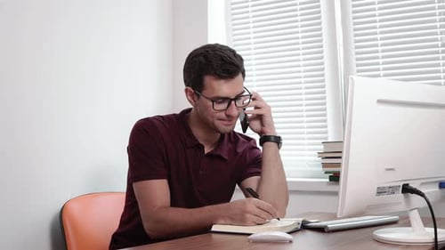Man Taking Notes on a Phone Call in Office