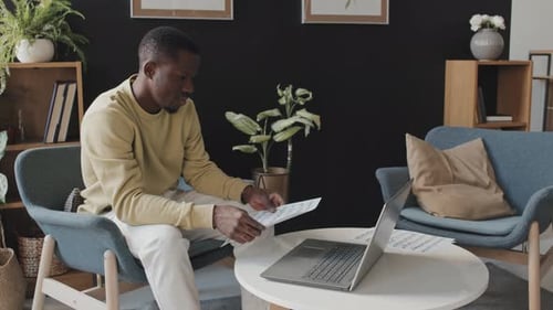 Man with Sheet Music Uses Laptop Indoors