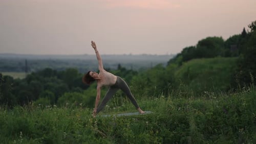 Woman Practices Yoga in a Green Field at Sunset