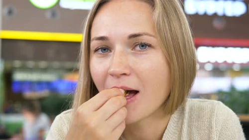 Woman Eats French Fries and Smiles Sitting in Mall Cafe