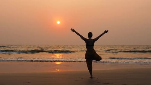 Young Healthy Woman Practicing Yoga on the Beach at Sunset