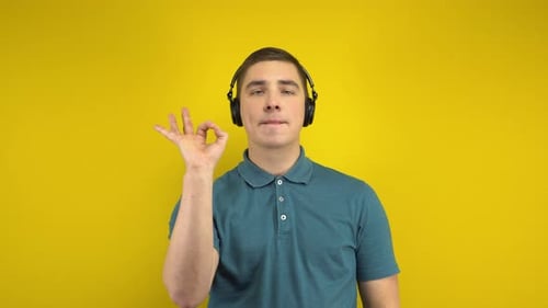 Young Man Dancing with Headphones on a Yellow Background. A Man in a Green Polo Is Listening To