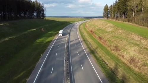 Aerial view of a white truck with a trailer driving along a scenic highway in the forest.