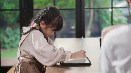 Girl Uses Tablet at Table by Window