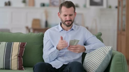 Concerned Man Counting Money on Green Couch