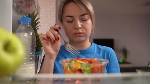 Woman Eating Salad from Inside Refrigerator
