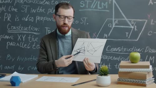 Man Explaining Math at Desk in Front of Chalkboard