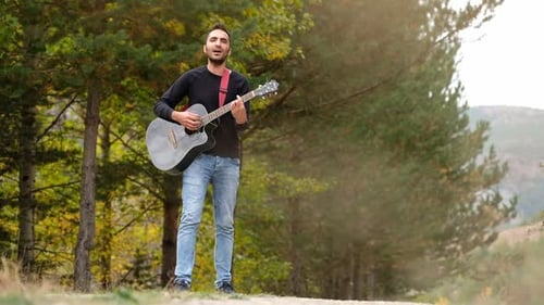 Joven toca la guitarra y canta en el bosque