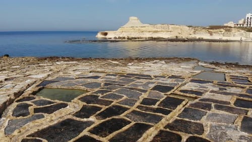 An aerial drone shot slowly pans across the rock-cut Salt Pans and beautiful coast of Gozo Island in