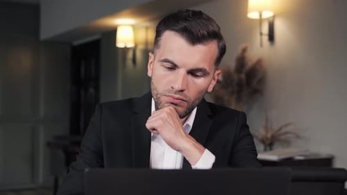 Thoughtful Stylish Businessman Working on Laptop Computer in Hotel Restaurant
