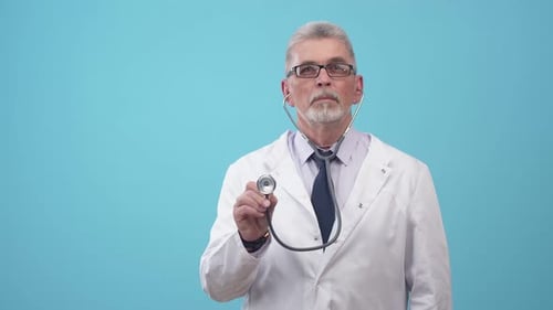 Adult Man Doctor in Medical Uniform and Glasses Listens with Stethoscope Standing in the Studio on a