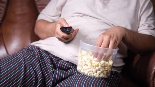 Person Eats Popcorn and Watches Television at Home