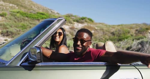 Portrait of african american couple waving and having fun while sitting in the convertible car on ro