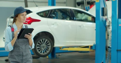 Mechanic Woman with Tablet Walking Along Car Workshop. Car Service, Repair, Maintenance and People