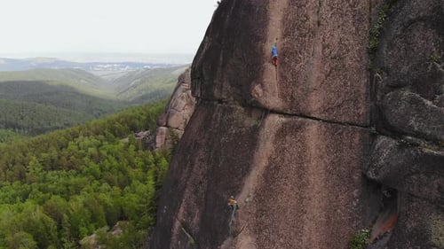 Rock Climbers Climbing Cliff Face Amidst Forest