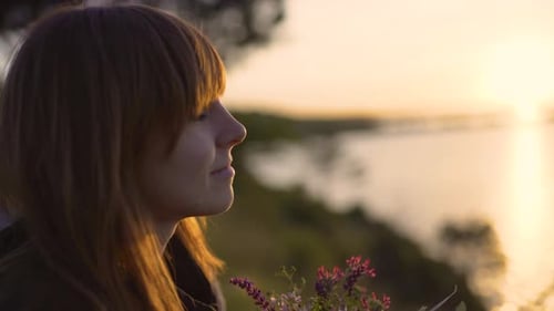 Schöne junge Frau mit einem Strauß Wildblumen an der Küste bei Sonnenuntergang