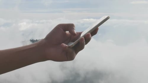 Hand Using Mobile Device above the Clouds