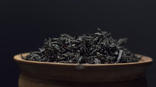 Close up view dry black ceylon tea leaves rotate in a clay bowl on black background