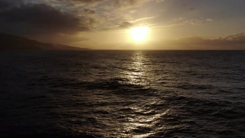 Drone flying low over the ocean towards the sun at sunset