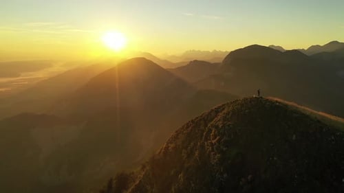 Lone Figure Standing on Mountain Peak at Sunrise