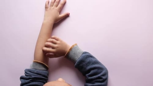 Child Scratching Arm on Pink Background