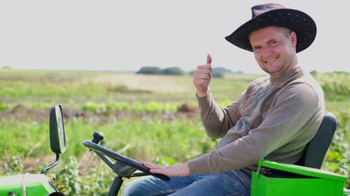 Portrait of Smiling Young Bearded Farmer Sitting on Small Farm Tractor