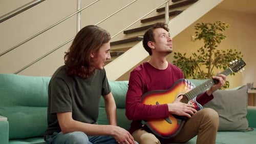 Man Plays Guitar for Friend on Sofa