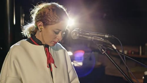 Woman Singing into Microphones Under Bright Spotlight