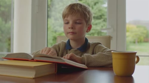 School Kid Reading Paper Book Sitting Alone at the Table at Home