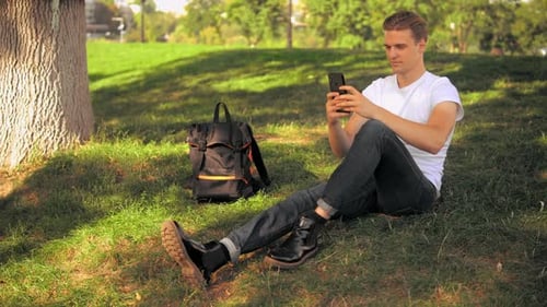 Young Man Using Phone While Sitting in Park