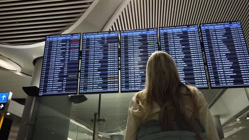 Woman in International Airport Looking at the Flight Information Board