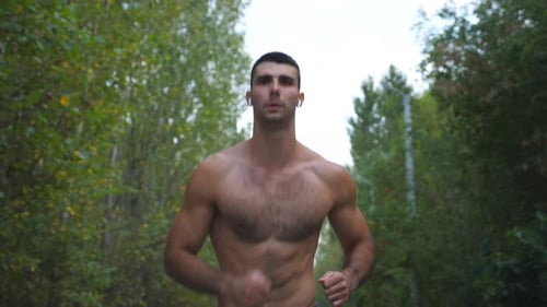 Muscular Sportsman with Wireless Headphones Running Along Road