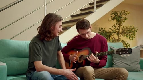 Young Adults Playing Guitar Together on Sofa