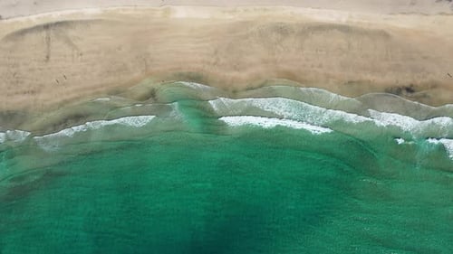 Fly over Kvalvika beach with splashing sea waves