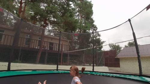 Girl Jumps on Trampoline Outdoors in Backyard