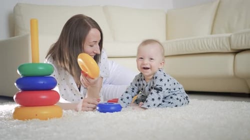 Joyful Mother and Baby Playing with Toys on a Carpet at Home. Side View of a Happy Mother and Son