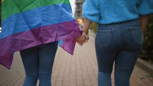 Couple Holding Hands with Rainbow Flag Walking on Street