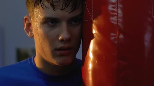 Boxeur adolescent fatigué regardant la caméra debout près du sac de frappe, le sport va alimenter