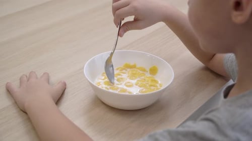 Over the shoulder view of a little boy eating cereal with milk for breakfast.