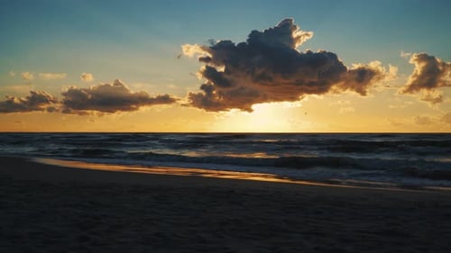 Sonnenuntergang hinter Wolken über Meereswellen und Sandstrand