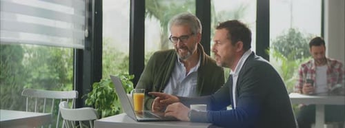 Deux hommes souriants au café au-dessus d'un ordinateur portable