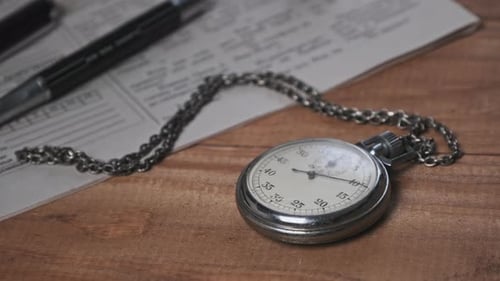 Vintage Stopwatch Lies on Wooden Desk with Old Documents and Counts Seconds